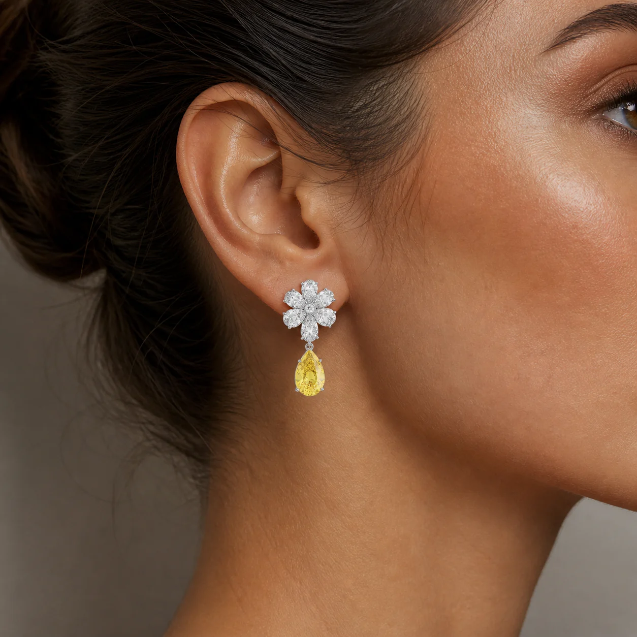 Yellow drop earrings with luminous white floral stones and a radiant pear-shaped drop worn close to the face