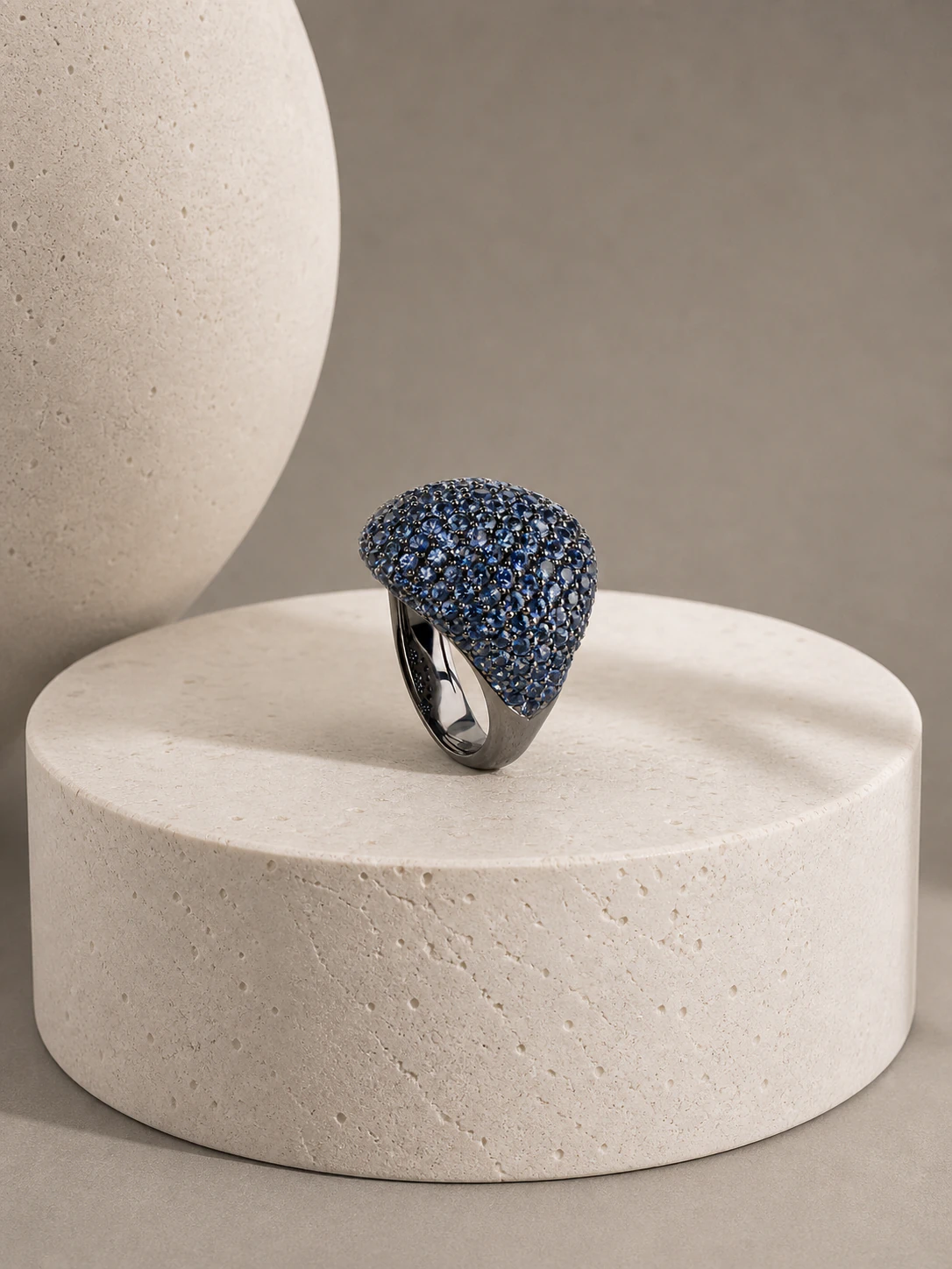 Blue gemstone cocktail ring displayed on a sculptural stone pedestal